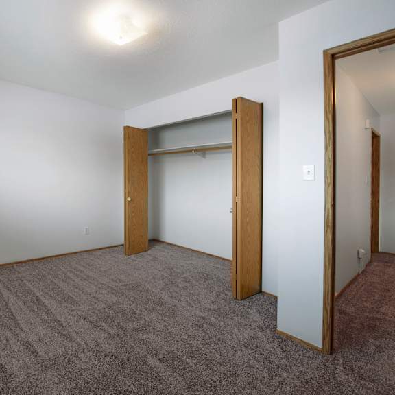a simple, bright bedroom here at willowview terrace with soft carpeting, white walls, and a ceiling light for even lighting. an open closet with wood sliding doors and a hanging rod provides practical storage, with a hallway entrance off to the side for an easy layout.