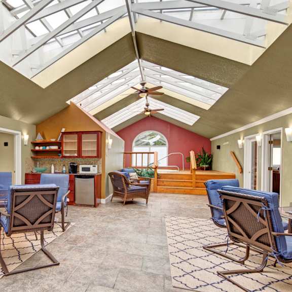 bright sunroom here at the club at eagle pointe apartments with skylights, wicker furniture with blue cushions, patterned rugs, a kitchenette with a microwave, and a calming hot tub area.