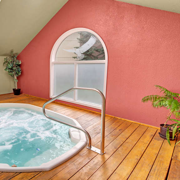 indoor jacuzzi here at the club at eagle pointe apartments with bubbling water on wooden flooring, next to a large, arched window. plants decorate the space, conveying a relaxing atmosphere.