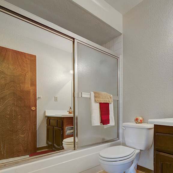 modern bathroom here at the continental apartments with a tiled shower, glass door, and white sink. a towel hangs over the shower door, and the vanity features a large mirror and lights.