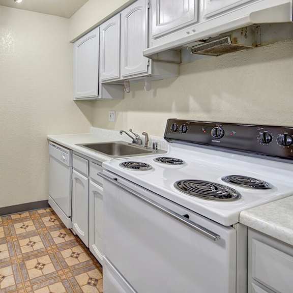 narrow kitchen here at the continental apartments with white cabinets, electric stove, sink, and refrigerator. beige walls and patterned vinyl flooring add a simple, clean look.