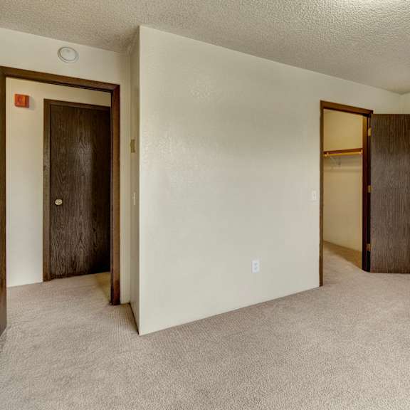 a spacious, empty room here at deer park apartments with light beige carpet and neutral walls, featuring two closed wooden doors leading to closets.