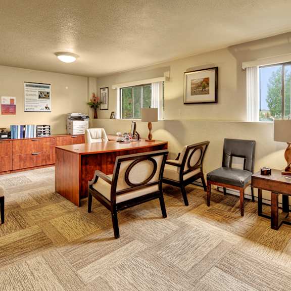 a well-lit office space here at deer park apartments featuring a wooden desk, comfortable seating, and large windows with a view of greenery outside.