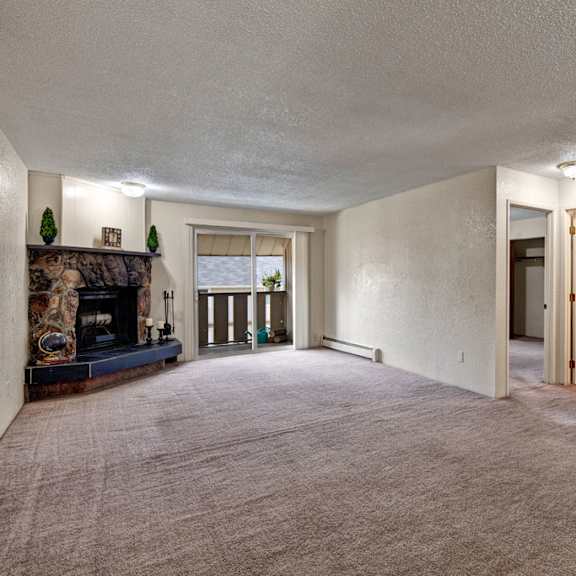 spacious living room here at greenbriar apartments with light beige carpet, stone fireplace, sliding glass doors, and open doorways. cozy and inviting with natural light.