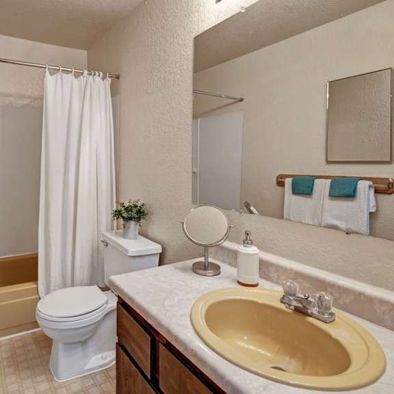 bathroom here at greenbriar apartments with a yellow bathtub and sink, white shower curtain, and countertop. towels and a small plant add color. clean and neutral decor.