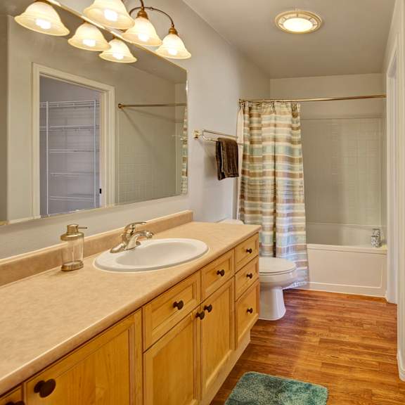 cozy bathroom here at the highlands luxury apartments with a wooden vanity, oval sink, and mirror. bathtub with a striped curtain, towel rack, washer, and wood floor. bright and clean.