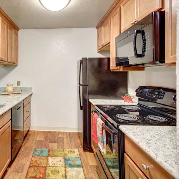 modern kitchen here at hillside chalet apartments with light wood cabinets, granite countertops, and stainless steel appliances. a colorful rug adds warmth, with an inviting, tidy feel.