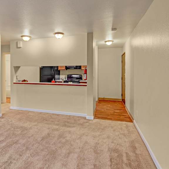 quiet apartment interior here at hillside chalet apartments with beige carpeted living area leading to a small kitchen. warm lighting creates a cozy and inviting atmosphere.