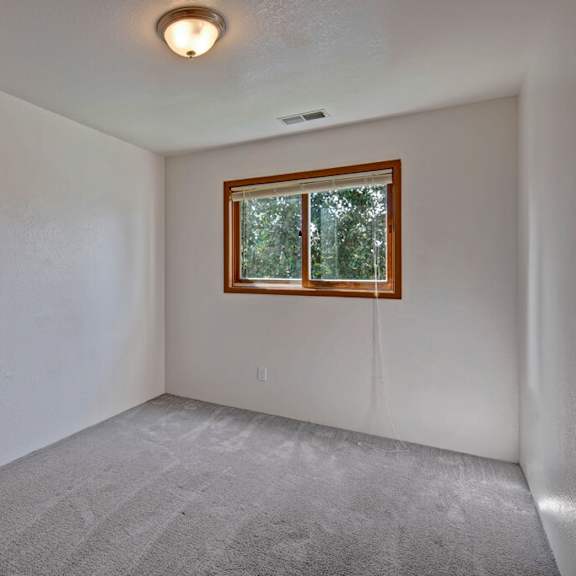 empty bedroom here at legacy west apartments with light gray carpet and white walls. a single window with wooden trim lets in natural light, creating a calm and simple ambiance.