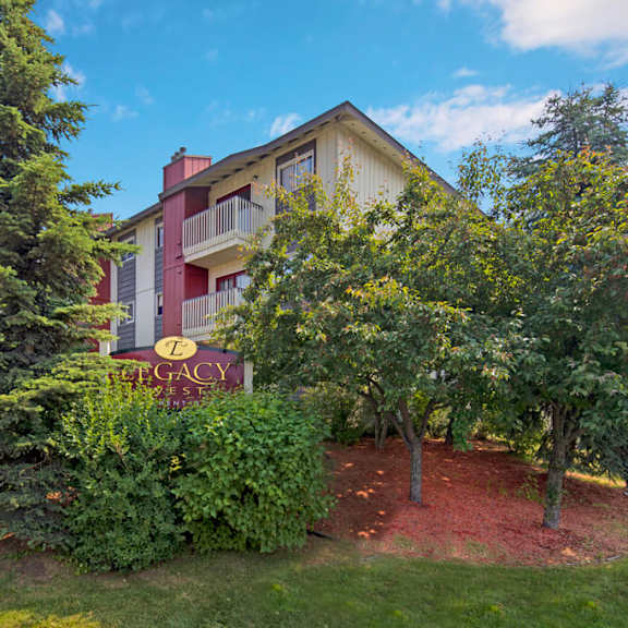 legacy west apartment building surrounded by lush trees and greenery under a blue sky. a sign reads "legacy" in the foreground, creating a peaceful ambiance.