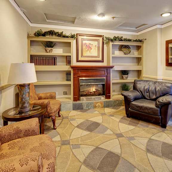cozy lounge area here at mendenhall tower apartments with a fireplace, flanked by a brown leather chair and floral-patterned sofas. bookshelves, a framed painting, and a mirror enhance warmth.