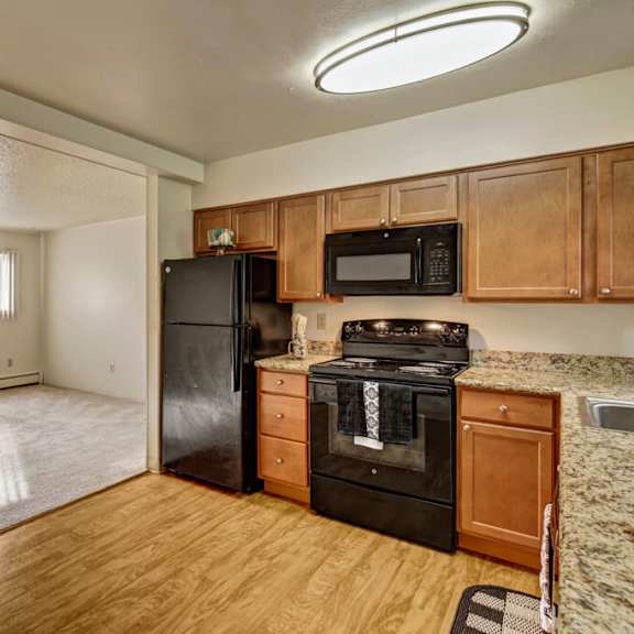cozy apartment interior here at montclair apartments with an open layout. the kitchen has wooden cabinets, black appliances, and a granite countertop. large window with blinds. bright and inviting.