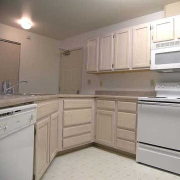 a bright kitchen here at brighton park with light wood cabinets, white appliances including a stove, microwave, and dishwasher. clean and functional design.