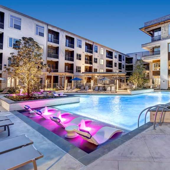 a swimming pool with purple lighting in the middle of a courtyard surrounded by buildings.