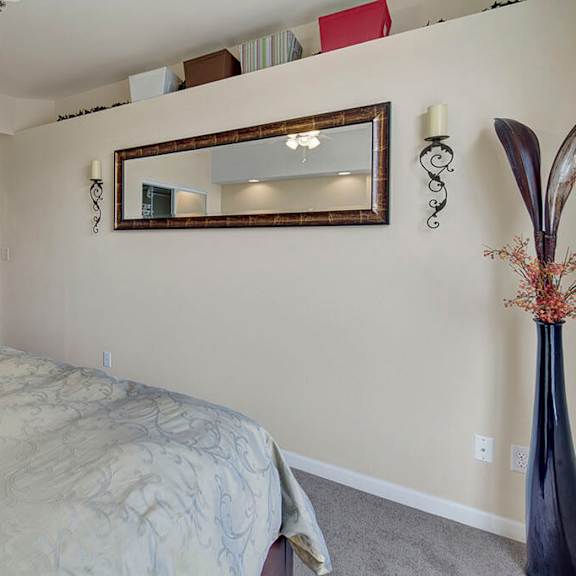 minimalist bedroom here at park plaza 2 apartments with a bed covered in a patterned comforter, a wall mirror, intricate metal sconces, and a tall vase with dried flowers, creating a serene ambiance.
