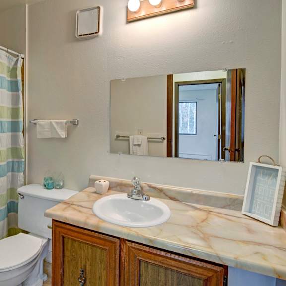 a bathroom here at park plaza apartments with a striped shower curtain in green, blue, and white. a marble sink counter holds soap and a decorative sign. bright, clean ambiance.