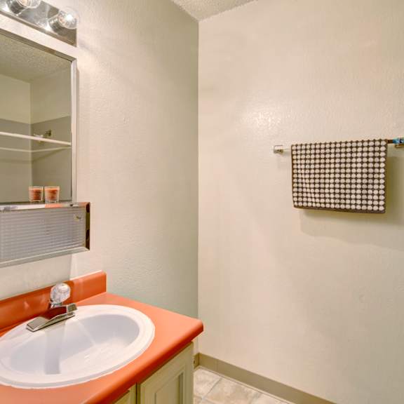 a small bathroom here at quiet creek apartments with a coral countertop sink, a lit mirror above, and a patterned towel on a rack. neutral tones create a clean, simple feel.