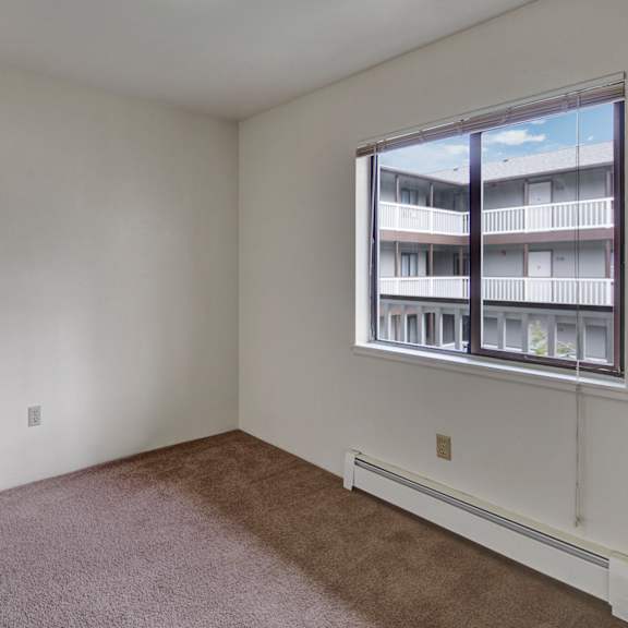 empty bedroom here at silver ridge apartments with beige carpet, white walls, and a window showing an apartment building courtyard. the light creates a calm, neutral tone.