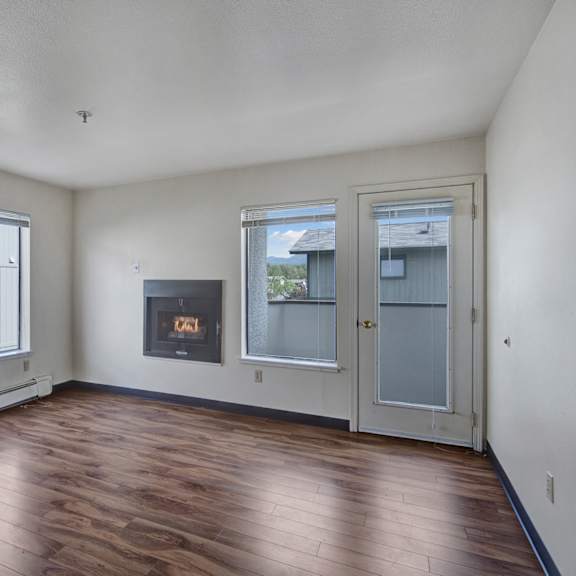 empty living room here at silver ridge apartments with light wood flooring, white walls, and a modern fireplace. large windows and a glass door provide natural light. cozy and minimalistic.