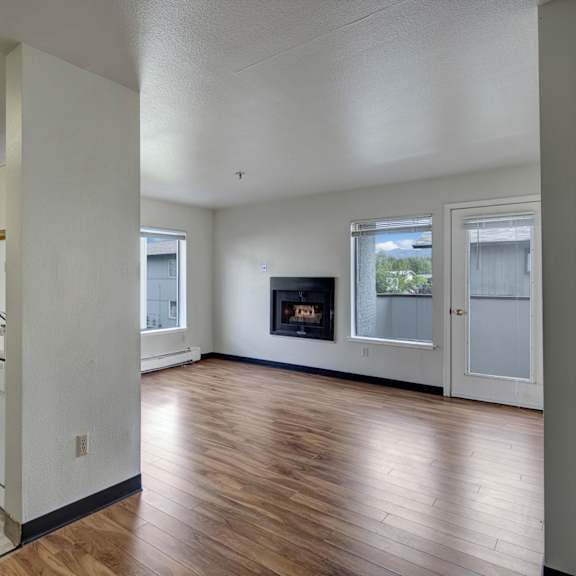 a small kitchen here at silver ridge apartments with light cabinets, white appliances, and a cozy rug opens into a bright living room with hardwood floors and a corner fireplace.