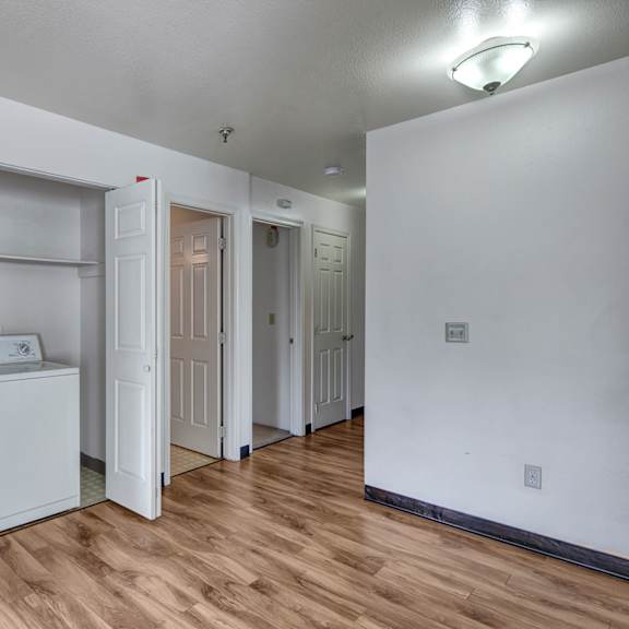 bright laundry area here at silver ridge apartments with white washer and dryer set against a light wall. wood flooring leads to open doors revealing more rooms, under soft overhead lighting.