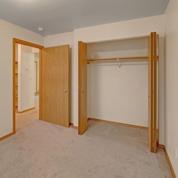 empty beige room here at strawberry lane apartments with an open closet on the right and a wooden door on the left. soft carpet flooring, simple and clean atmosphere.