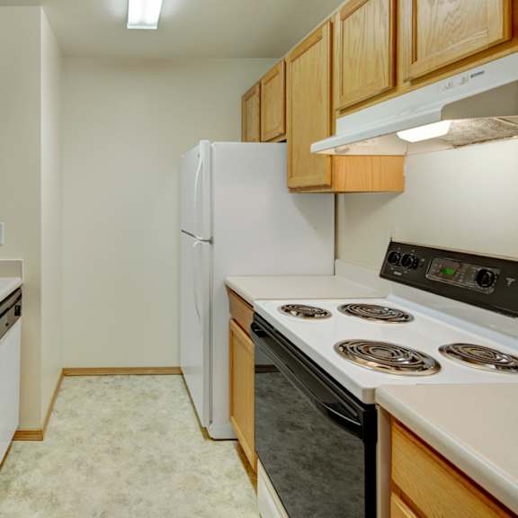 narrow kitchen here at strawberry lane apartments with wooden cabinets, white countertops, a double sink, electric stove, dishwasher, and fridge. bright, clean, and organized space.