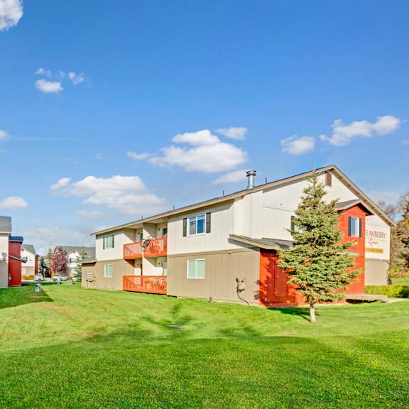 strawberry lane apartment buildings with beige and red accents are surrounded by green lawns and trees under a blue sky with scattered clouds, creating a peaceful suburban atmosphere.