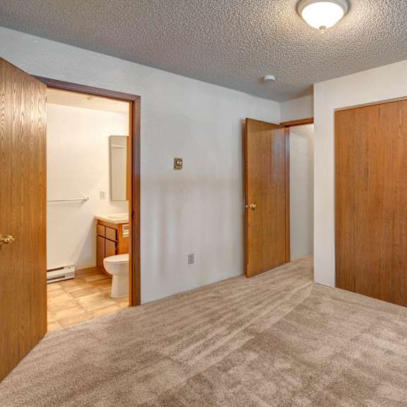 empty bedroom here at terrace on the lake apartments with beige carpet, a wooden closet with sliding doors, and an open door revealing a bathroom. soft lighting creates a neutral, calm tone.