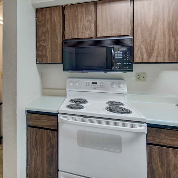 compact kitchen here at terrace on the lake apartments with white stove, dark wood cabinets, and built-in microwave. adjacent, a stacked washer and dryer in a small laundry nook.