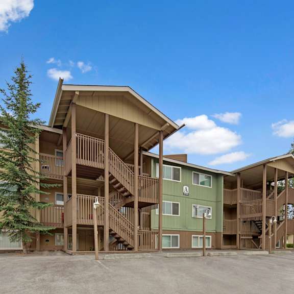 the club at eagle pointe apartments building with wooden exterior, green and beige tones. three-story structure with staircases, surrounded by trees under a clear blue sky.