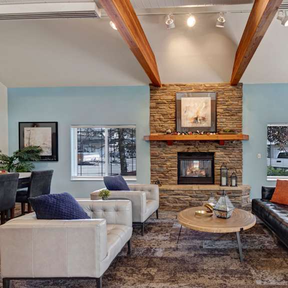 a cozy resident lounge here at the highlands luxury apartments with a stone fireplace, wooden beams, and modern furniture. soft lighting and pillows create a warm, inviting atmosphere.