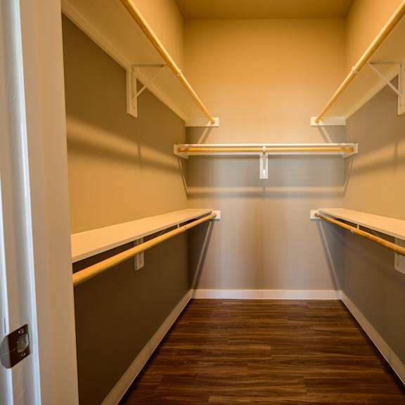 a spacious walk-in closet here at harmony luxury with warm wood-style flooring, neutral-toned walls, and built-in shelving with hanging rods on both sides, offering ample storage in a clean, organized, and well-lit space.