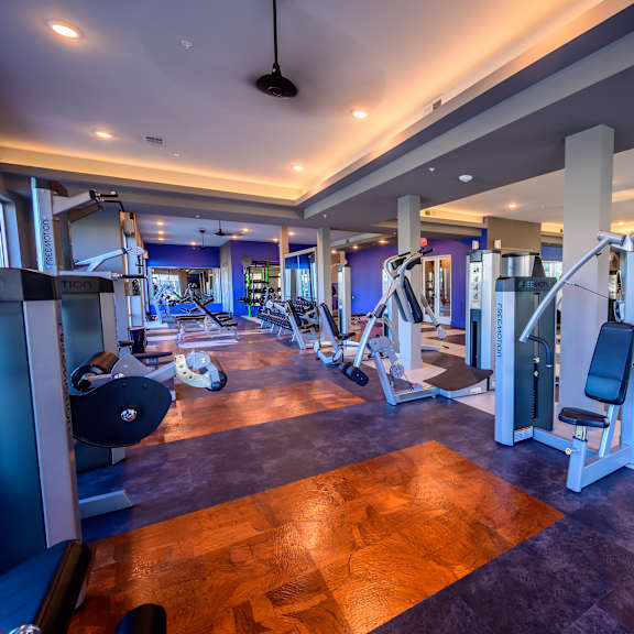 a spacious fitness center here at harmony luxury with a wide variety of modern strength and cardio equipment, polished flooring, tall columns, and recessed ceiling lighting, creating a bright, open, and energizing space for workouts.