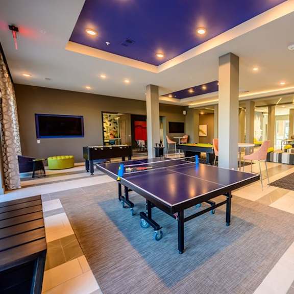 a modern game room here at harmony luxury featuring a ping pong table, pool tables, lounge seating, and mounted tvs, enhanced by stylish lighting, open layout, and a lively, social atmosphere for residents to enjoy.