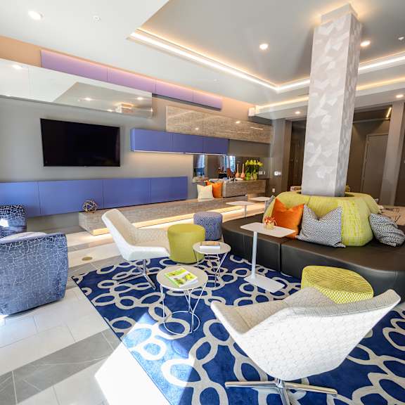 a modern community lounge here at harmony luxury with stylish seating, colorful accent pillows, a mounted tv, and sleek built-in shelving, enhanced by contemporary lighting and an open layout that creates a welcoming, upscale atmosphere for relaxing or socializing.