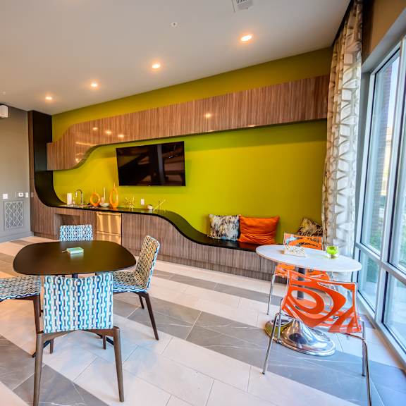 a vibrant community lounge here at harmony luxury with modern seating, colorful accent chairs, a built-in refreshment area, and a mounted tv, enhanced by natural light and contemporary design elements that create a fun, social atmosphere.