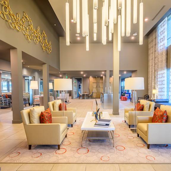 a spacious community lounge here at harmony luxury with plush seating, modern accent pillows, a central coffee table, and dramatic pendant lighting, enhanced by tall windows, soft neutral tones, and an elegant, welcoming atmosphere.