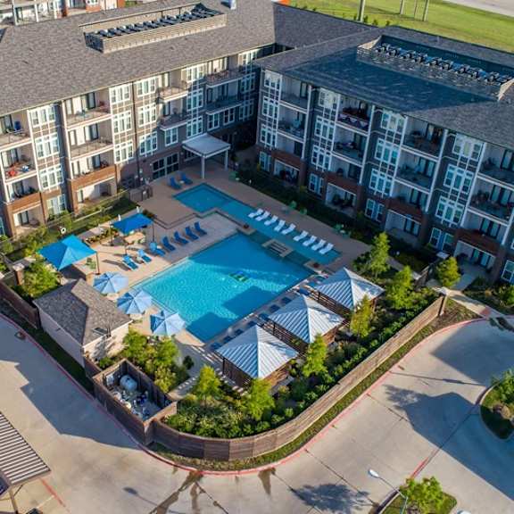 aerial view here at harmony luxury showcasing a resort-style pool courtyard with in-water lounge chairs, poolside seating, shaded cabanas, and landscaped greenery, surrounded by modern multi-story apartment buildings for a vibrant, upscale community setting.