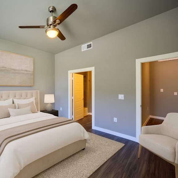 a serene bedroom here at harmony luxury with a plush upholstered bed, soft neutral bedding, and matching bedside tables, complemented by a ceiling fan, warm accent lighting, and an adjoining bathroom entry that creates a calm, upscale retreat.