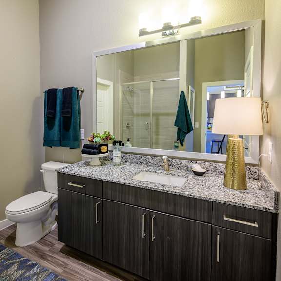 a stylish bathroom here at harmony luxury with a wide granite countertop, dark wood vanity, and a large framed mirror, featuring modern lighting, a sleek sink, and a glass-enclosed shower that adds a clean, upscale feel.