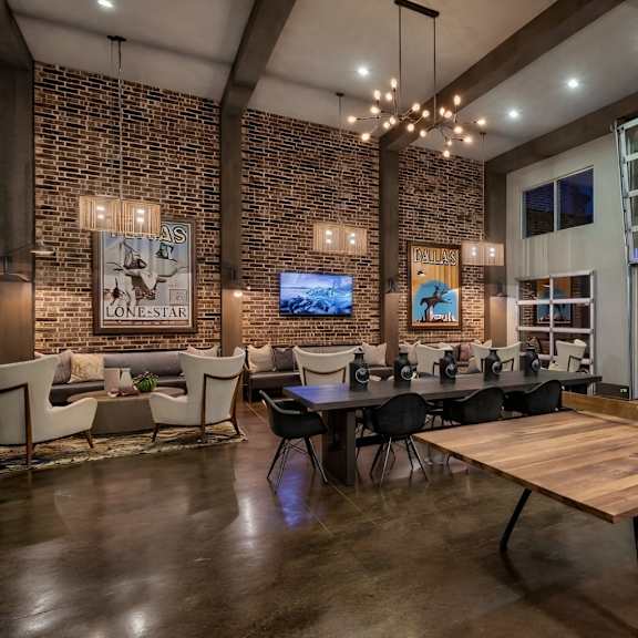 a resident lounge here at skyline farmers market with brick accent walls, dark wood beams, long community table, wood table tennis table, warm chandelier lighting, and modern seating areas opening to an outdoor pool patio.