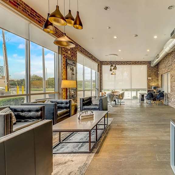 a business lounge here at skyline farmers market with black leather sofas, warm wood floors, brick walls, gold pendant lights, large windows, shared work tables, and a long desk workspace along the wall.