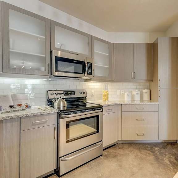 a kitchen here at skyline farmers market with light wood cabinets, stainless steel stove and microwave, white tile backsplash, granite counters, and polished concrete floors in a bright, modern layout.