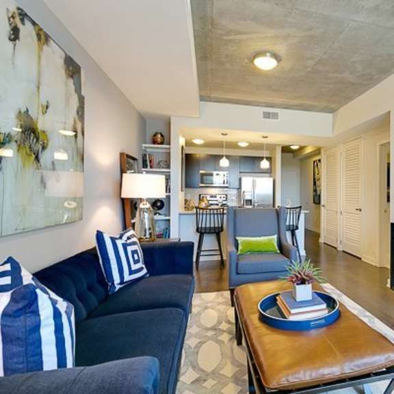 a stylish living room here at victory place with dark wood flooring, a blue sofa with patterned pillows, a coffee table, modern artwork, and an open view toward the kitchen with bar seating and pendant lights.