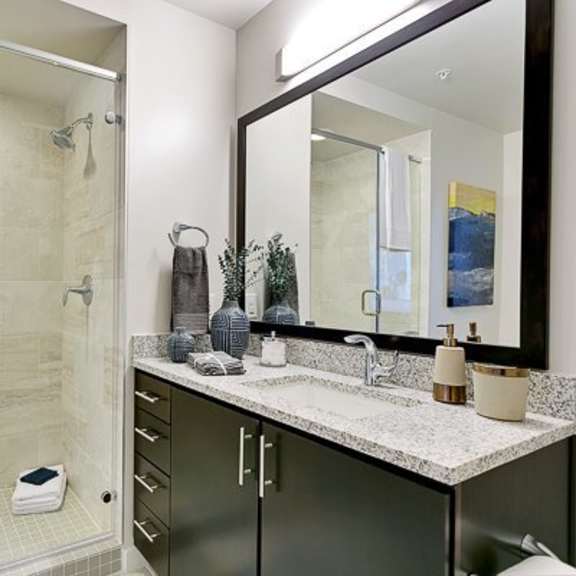 a bathroom here at victory place with a walk-in shower and a dark-wood, modern sink vanity.