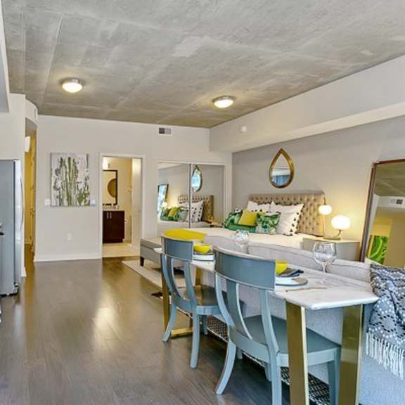 a modern open kitchen and studio layout here at victory place with dark cabinets, stainless steel appliances, a dining table for four, and a cozy sleeping and seating area with green accent decor.