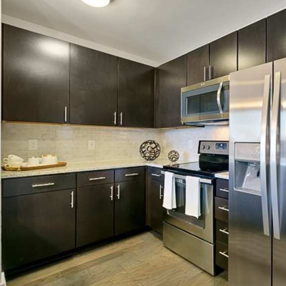 a modern corner kitchen here at victory place with dark cabinets, stainless steel appliances, a side-by-side refrigerator, microwave and oven range, and light countertops with a clean, polished look.