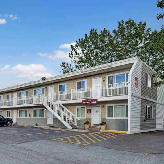 two-story village at calais apartment building with a staircase in the center, surrounded by parked cars. clear blue sky, trees in the background; welcoming, calm atmosphere.