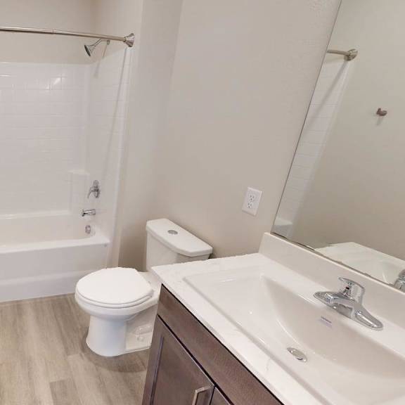 a clean modern bathroom here at autumn haus featuring a tub and shower combination with white tile surround, a single vanity with a smooth countertop and integrated sink, a large wall mirror, neutral walls, wood-style flooring, and simple fixtures that create a bright, functional, and uncluttered space.